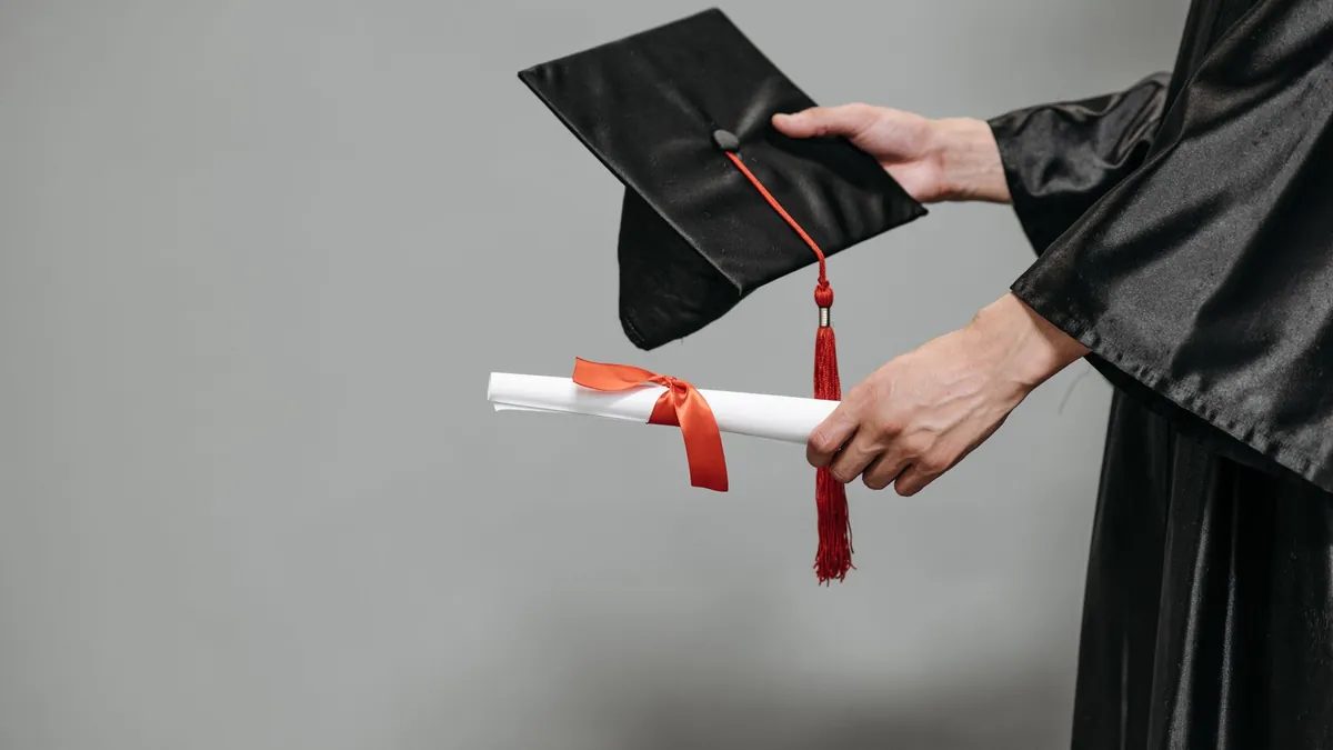 Persona sosteniendo un birrete y un diploma de graduación